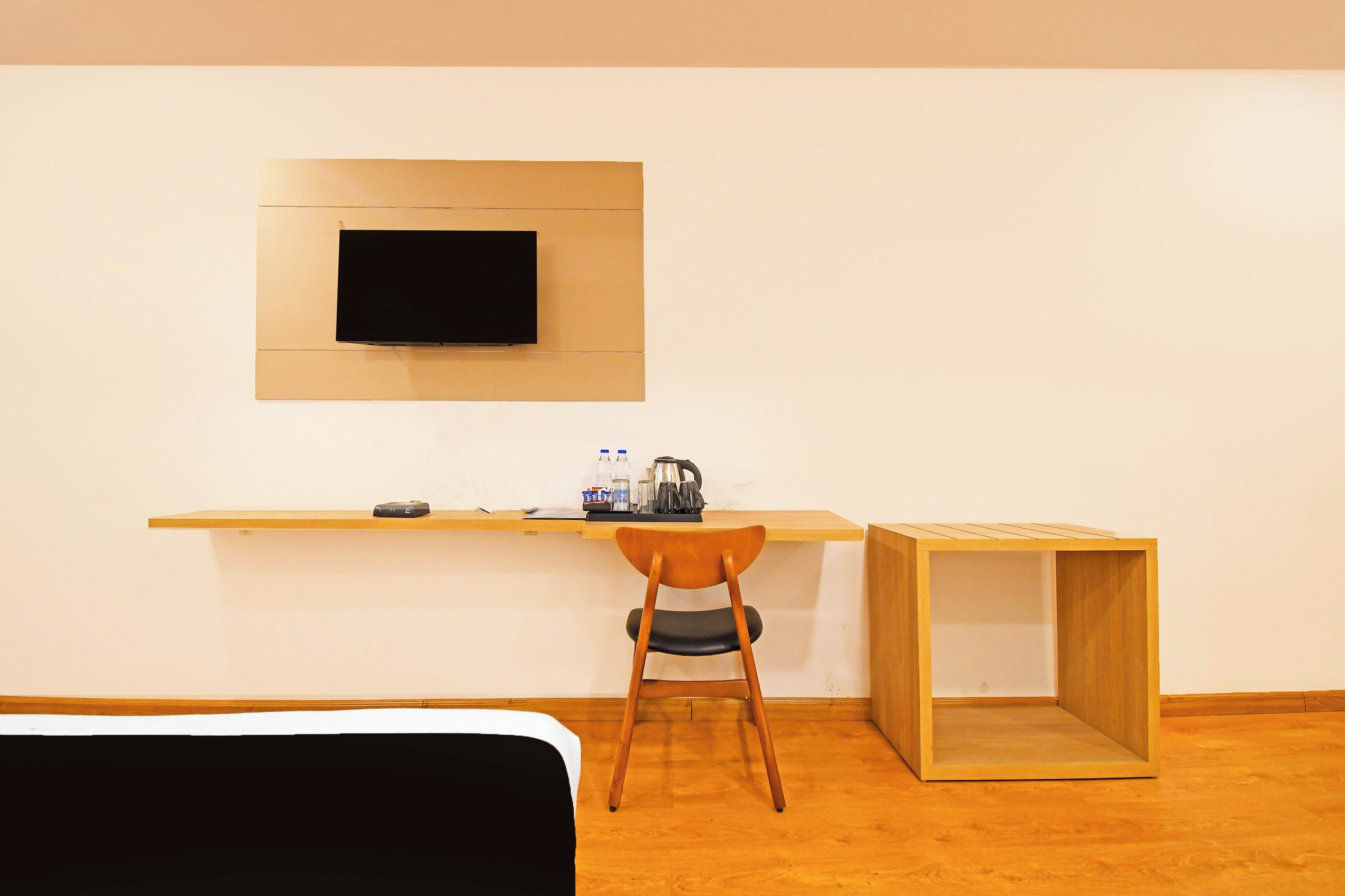 A room with a bed, a desk with a chair, a television mounted on the wall, and a small wooden table.