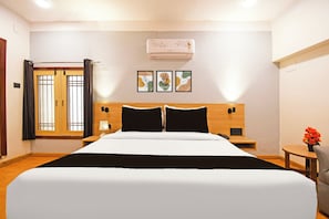 Habitación de hotel con una cama grande, una mesita de noche con una lámpara, una pequeña mesa con un florero y un aire acondicionado de pared.