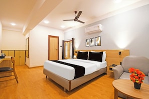 Una habitación de hotel con una cama, una silla, una mesita con un jarrón de flores, un ventilador de techo y un equipo de aire acondicionado.