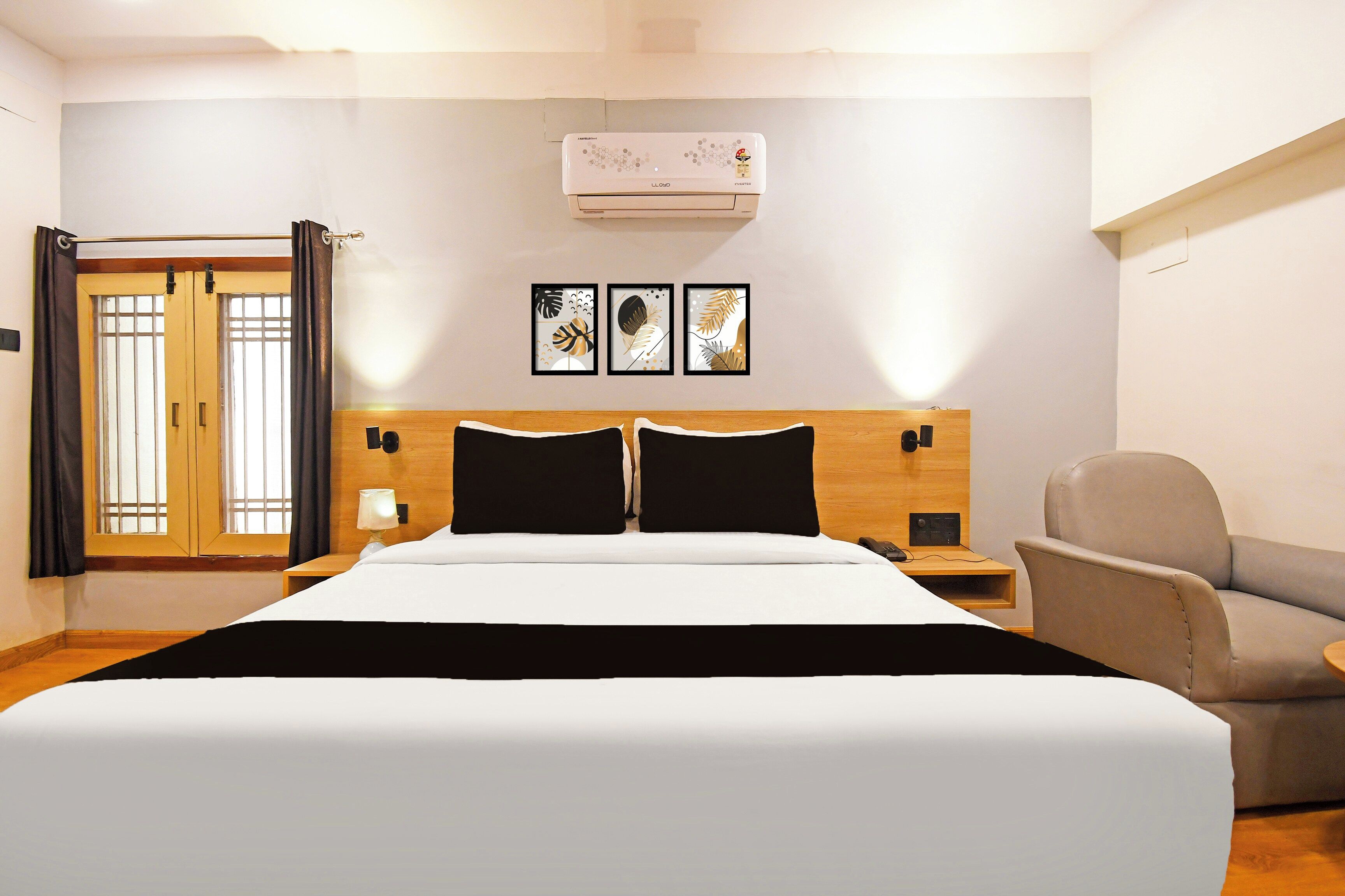 Habitación de hotel con cama, una silla, mesita de noche, lámpara y aire acondicionado instalado en la pared.