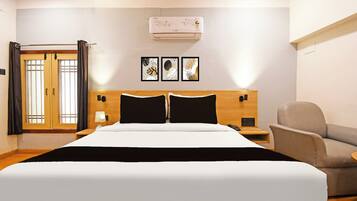 Habitación de hotel con cama, una silla, mesita de noche, lámpara y aire acondicionado instalado en la pared.