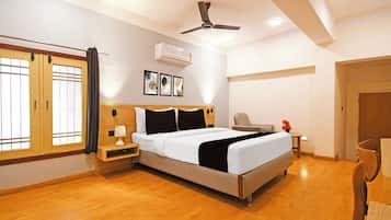 Une chambre d’hôtel comprenant un lit, une table de chevet, une lampe, un climatiseur, un ventilateur de plafond, des œuvres d’art et une fenêtre avec des rideaux.