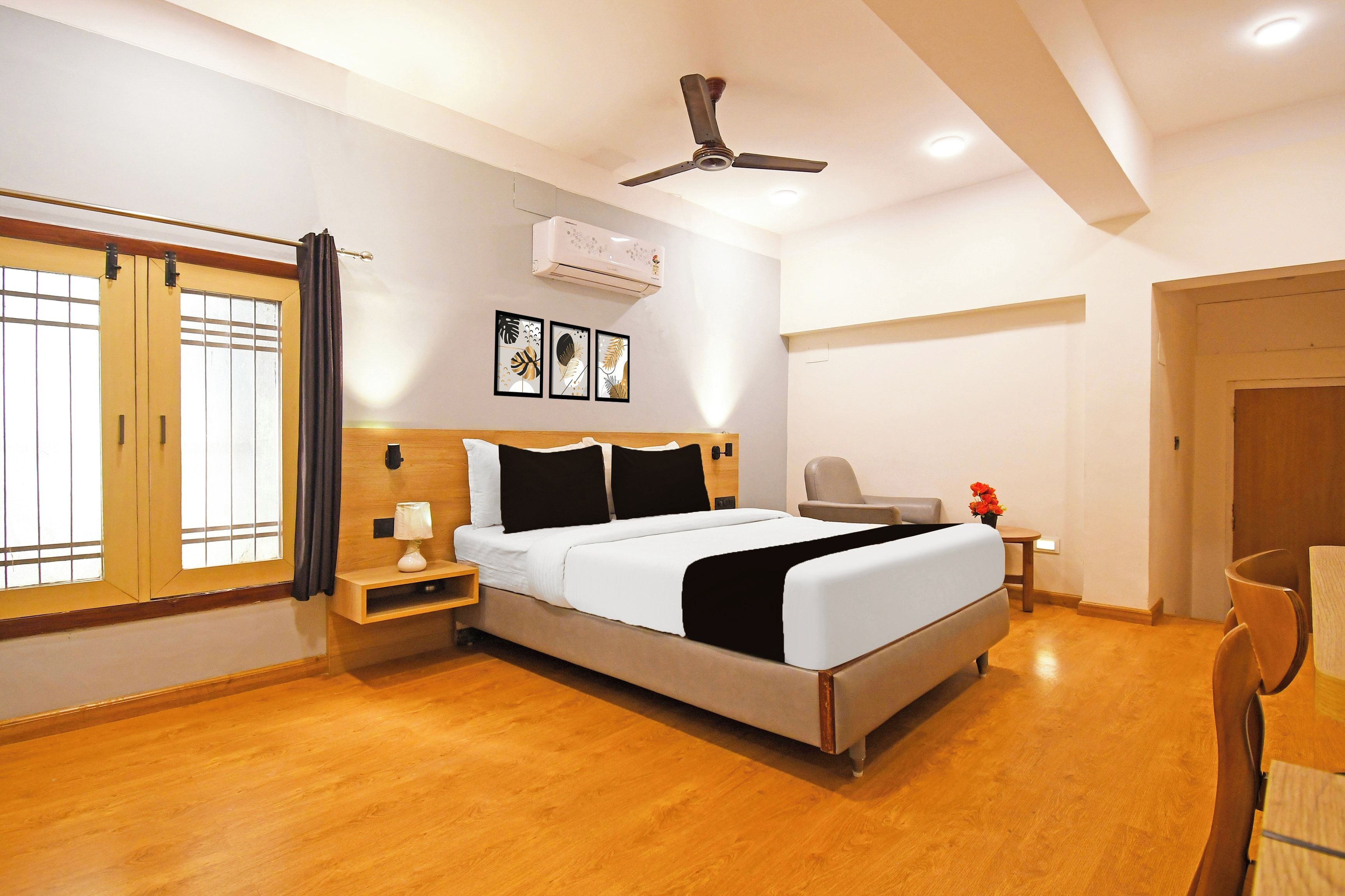 A hotel room with a bed, bedside table, lamp, air conditioning unit, ceiling fan, and a window with curtains.