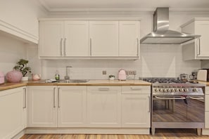 A kitchen with white cabinetry, a stainless steel range hood, and a wooden countertop. - Yule House - North East Escapes (Alnwick)