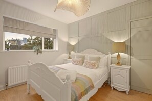 A bedroom with a large bed, bedside tables, a radiator, and a window with a view of buildings. - Yule House - North East Escapes (Alnwick)