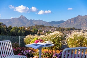 A terrace with a table and chairs, overlooking a town and mountains.