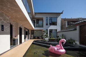 Un edificio moderno con piscina, un flotador de flamenco rosa y arquitectura tradicional al fondo.