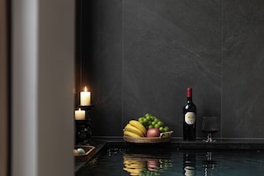 A dimly lit room with a reflective water surface, a candle, a bottle of wine, and a bowl of fruit.