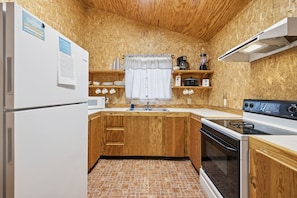 A compact kitchen with wooden cabinets, a built-in oven, a microwave, and a sink. - Riverside Cabins at Cypress Bend #3 @ (Concan)