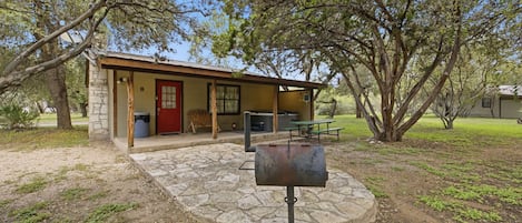A rustic cabin with a stone foundation, a red door, and a picnic table.