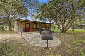 A rustic cabin with a stone foundation, a red door, and a picnic table. - Riverside Cabins at Cypress Bend #3 @ (Concan)