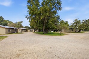 A campground with multiple cabins, a gravel parking area, and a large tree in the center. - Riverside Cabins at Cypress Bend #5 @ (Concan)