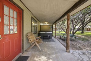 Eine überdachte Veranda mit roter Tür, einem Schaukelstuhl, einem Grill und Picknicktischen.