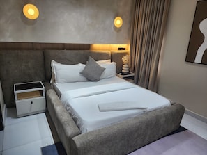A modern bedroom with a large bed, bedside tables, and a nightstand. - L Rina Apartment Brown unit (Lekki)