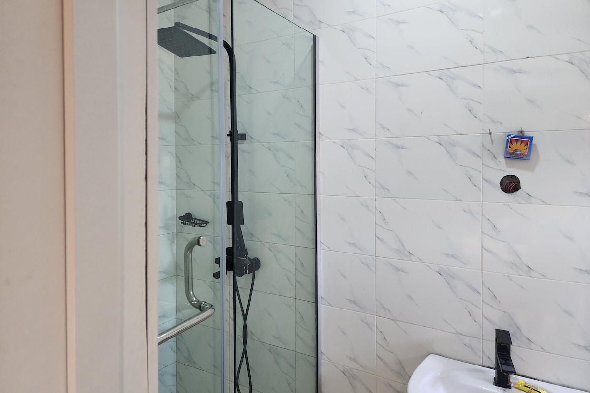 A glass-enclosed shower with a handheld showerhead and a handheld faucet.