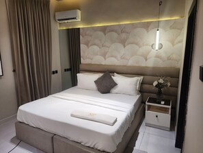 A hotel room with a bed, bedside table, and an air conditioning unit.