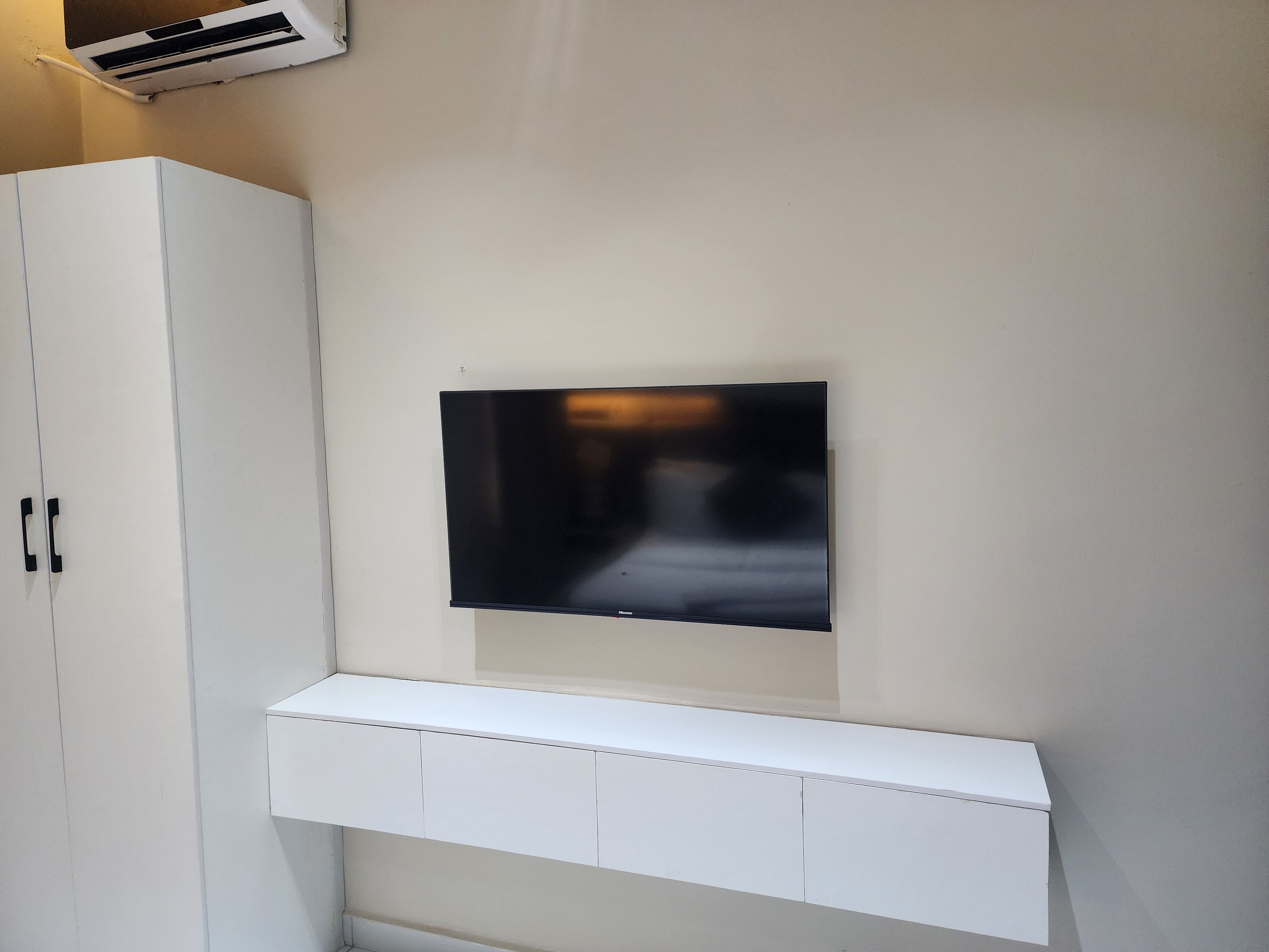 Un mur blanc orné d’un téléviseur à écran plat et, en dessous, d’un meuble blanc.