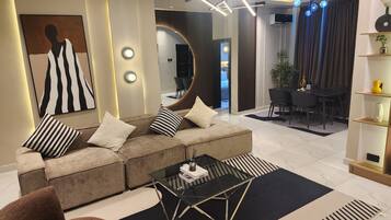 Un salon moderne avec un canapé d’angle, une table basse en verre et un coin repas comprenant une table et des chaises noires.