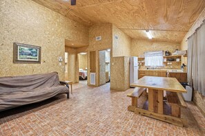 A room with a wooden floor, a sofa, a table, and a kitchen area with a refrigerator and sink. - Riverside Cabins at Cypress Bend #9 @ (Concan)