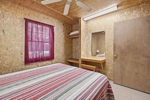 Ein Schlafzimmer mit Bett, einem Fenster mit Vorhängen, einem Holztisch, einem Spiegel und einer Tür.