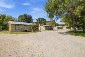 A row of single-story cabins with a gravel driveway, surrounded by trees. - Riverside Cabins at Cypress Bend #11 @ (Concan)