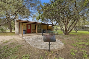 A rustic cabin with a stone foundation, a red door, and a picnic table. - Riverside Cabins at Cypress Bend #11 @ (Concan)