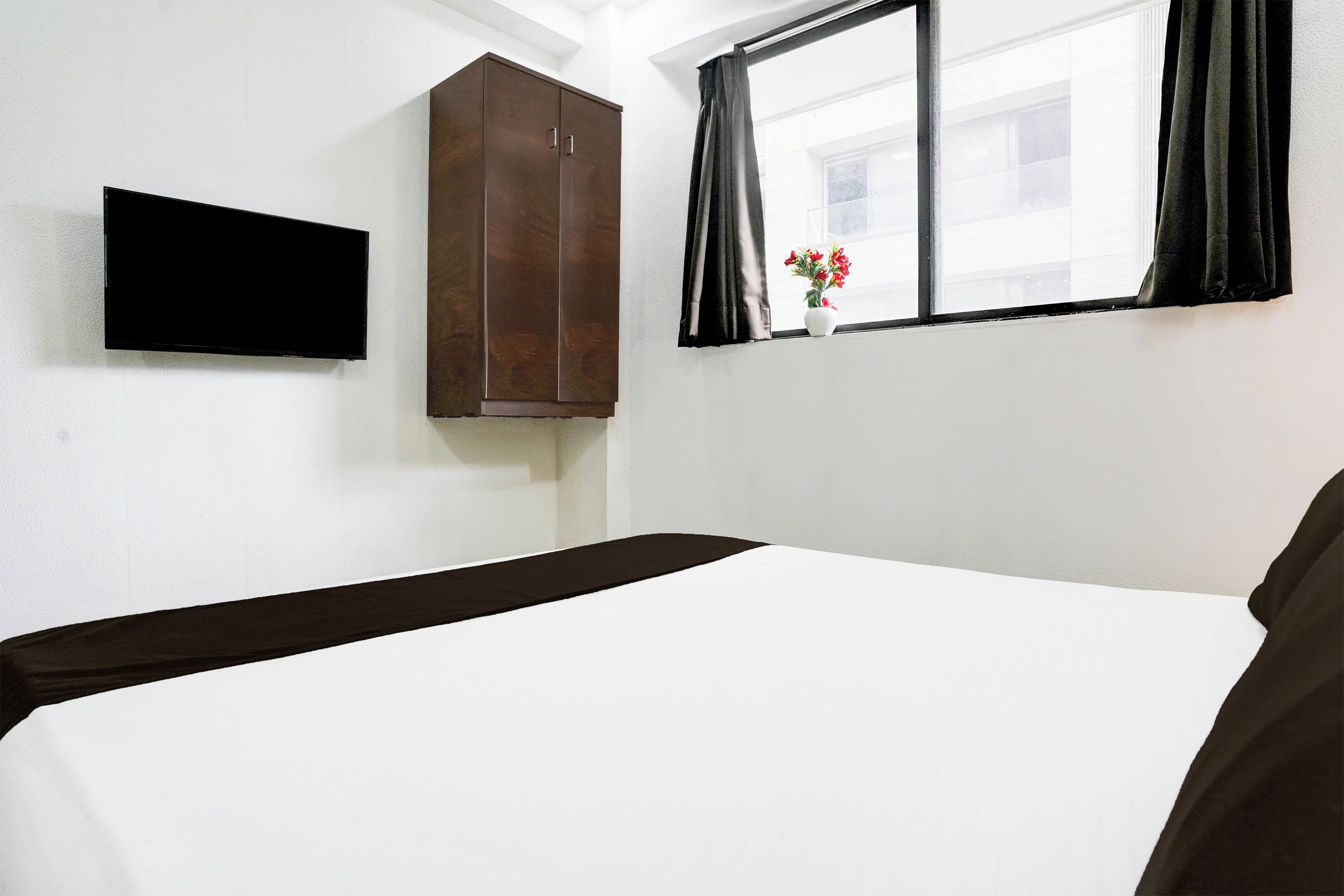 Una habitación de hotel con una cama, un televisor de pantalla plana montado en la pared, un armario y una ventana con cortinas.