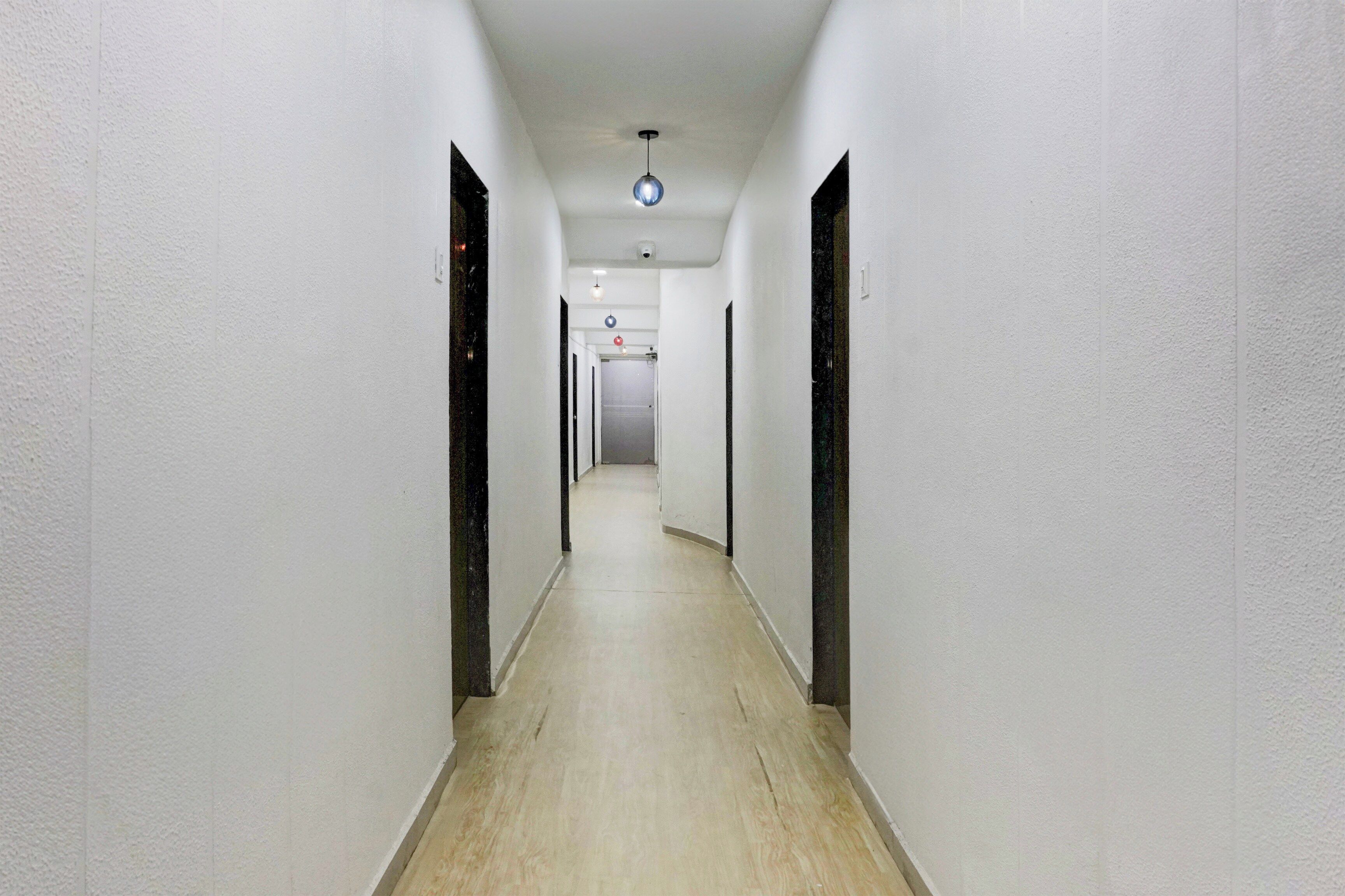 Un pasillo estrecho y bien iluminado, con paredes blancas y suelo de madera, que conduce a una puerta al final.