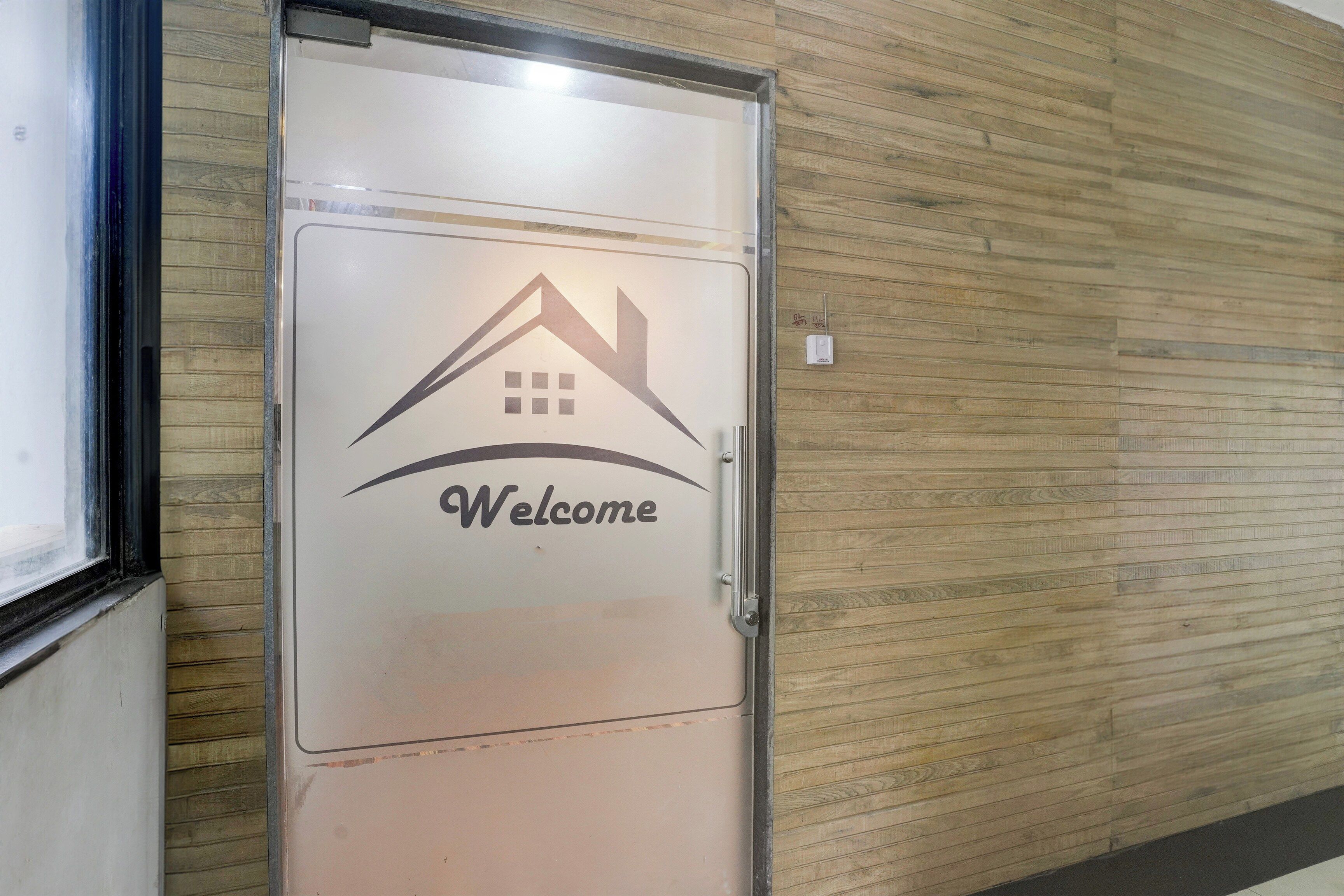 Una puerta con un letrero de bienvenida y un icono de casa, sobre un muro de madera.