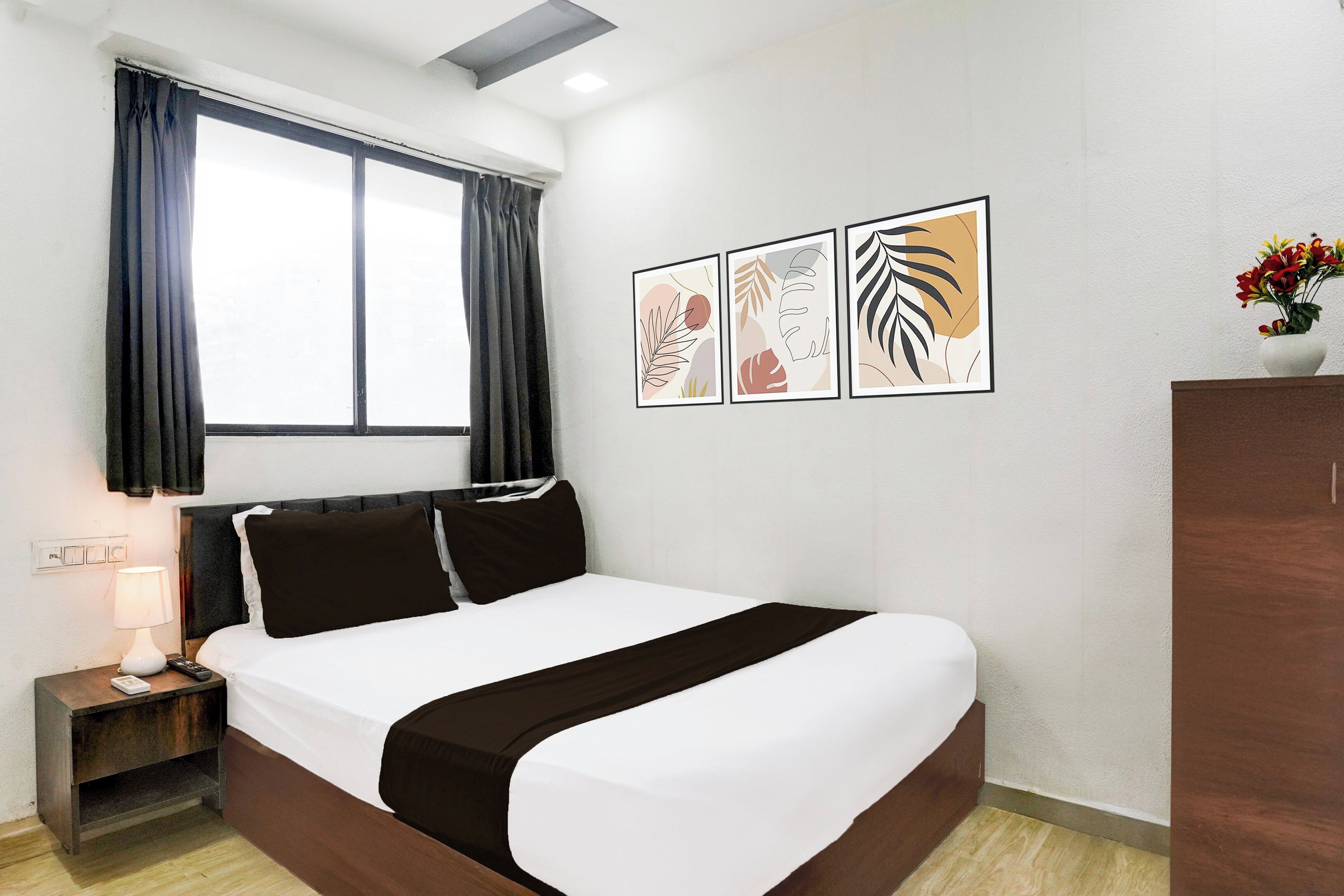 Een hotelkamer met een bed, nachtkastje, lamp, raam met gordijnen en wanddecoratie.