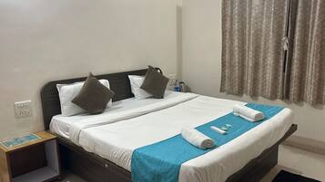 A neatly made bed with pillows, a blue towel, and a small table with a water bottle and a remote control.