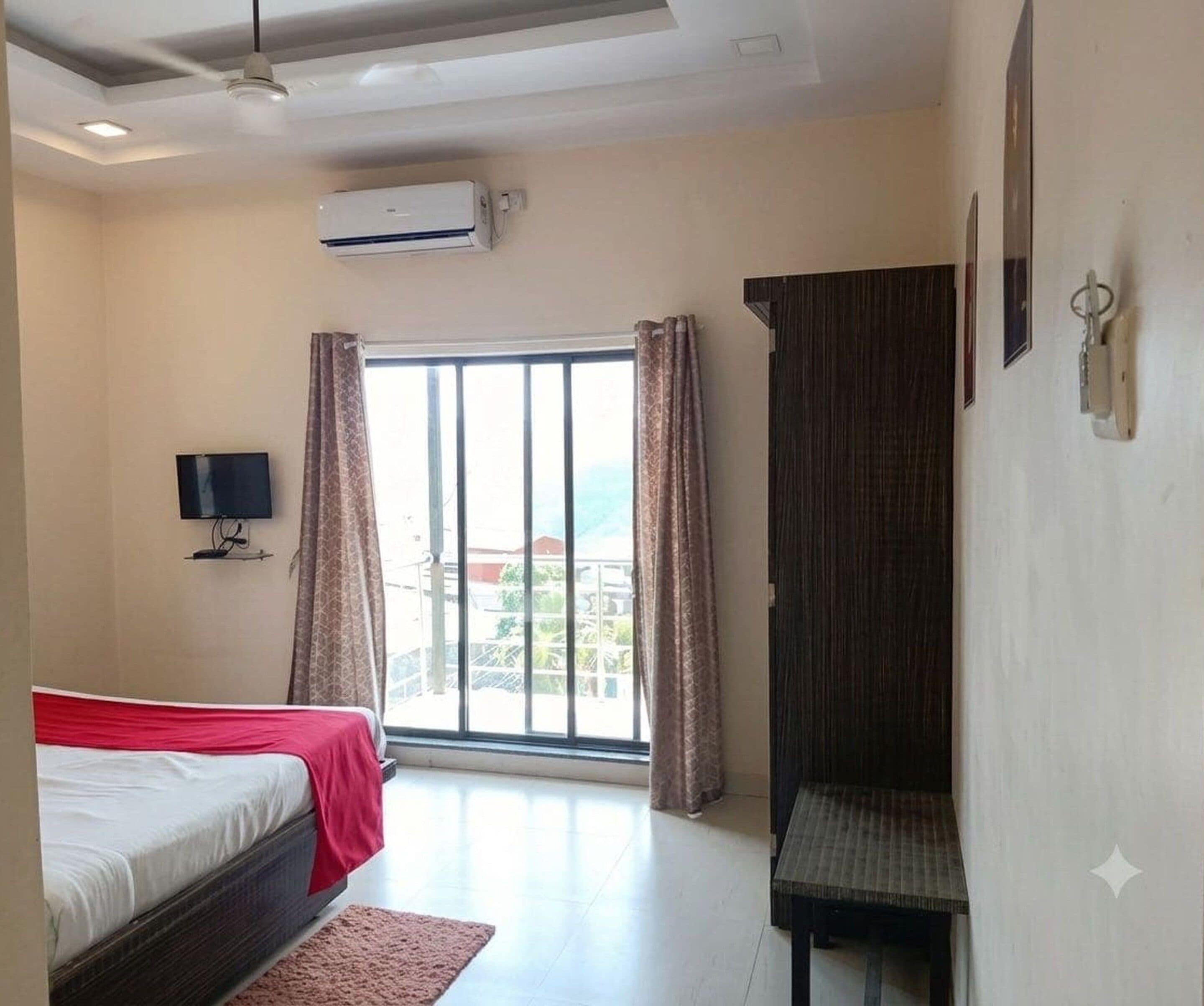 A hotel room with a bed, a TV, a desk, and a window with curtains.