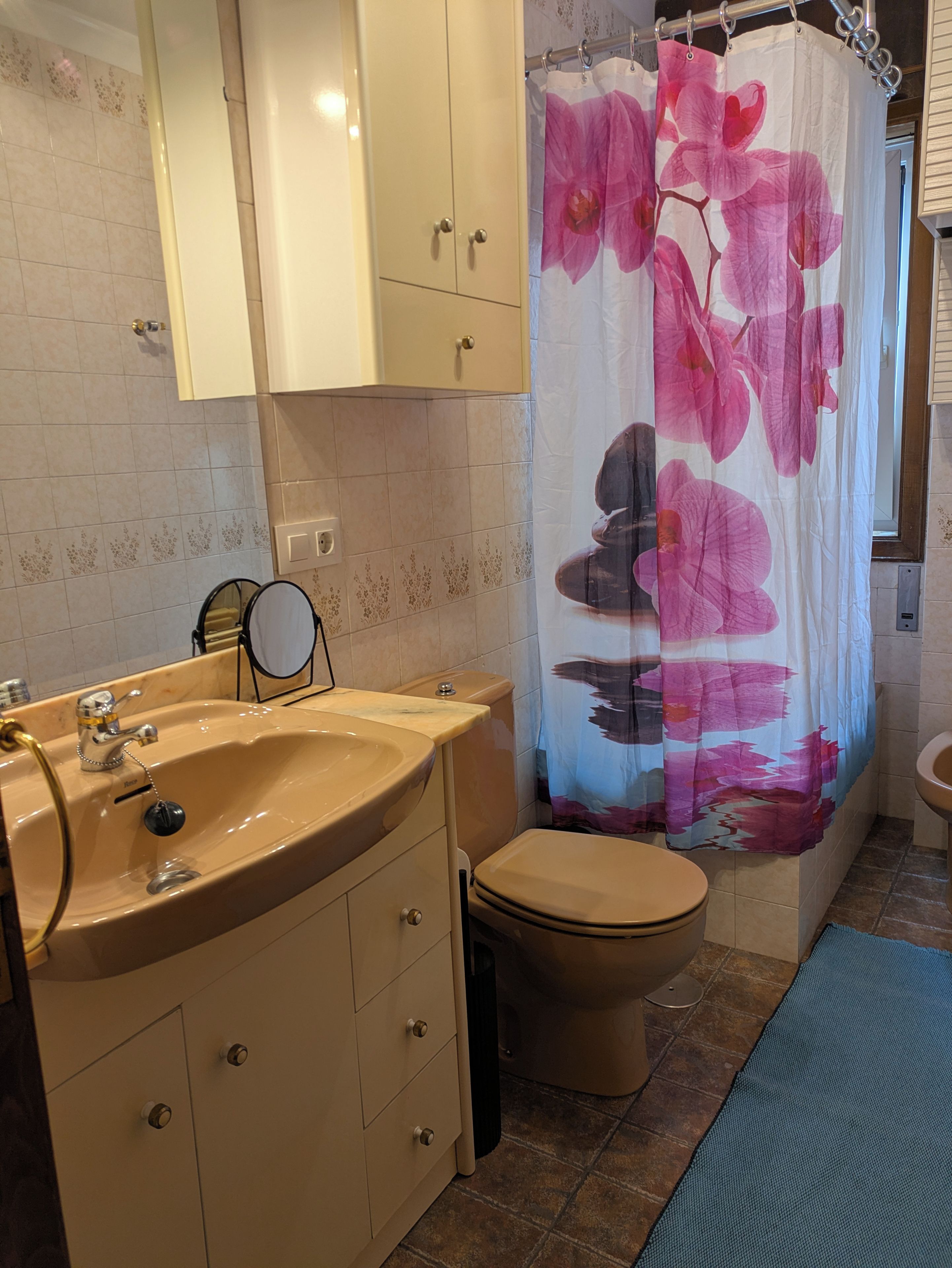 Ein Badezimmer mit einem beigen Waschbecken, einer Toilette und einem Duschvorhang mit Blumenmuster.