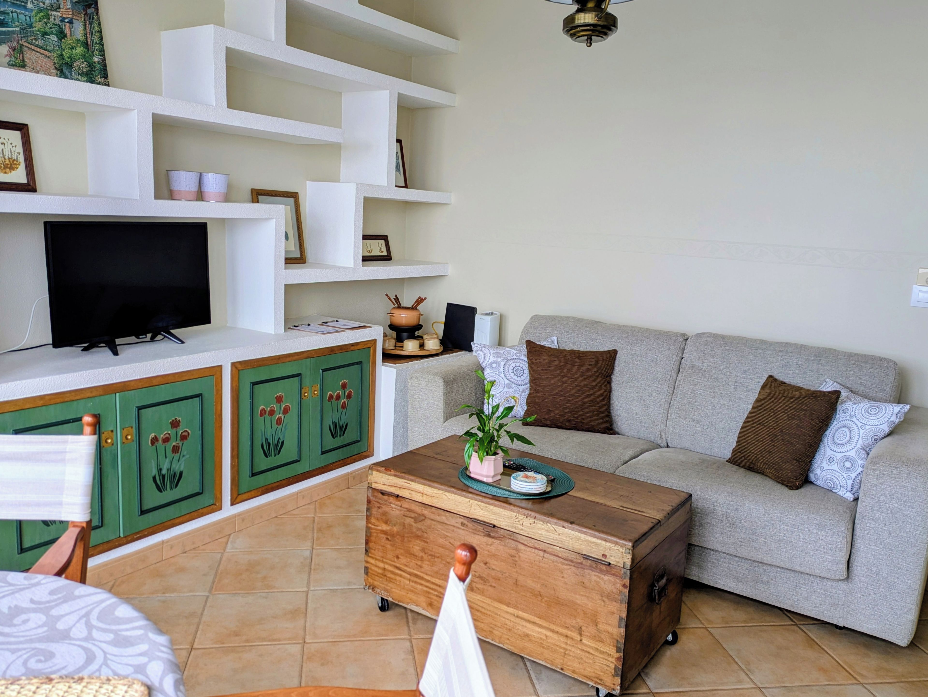 A living room with a sofa, a television, a wooden cabinet, and a tiled floor.