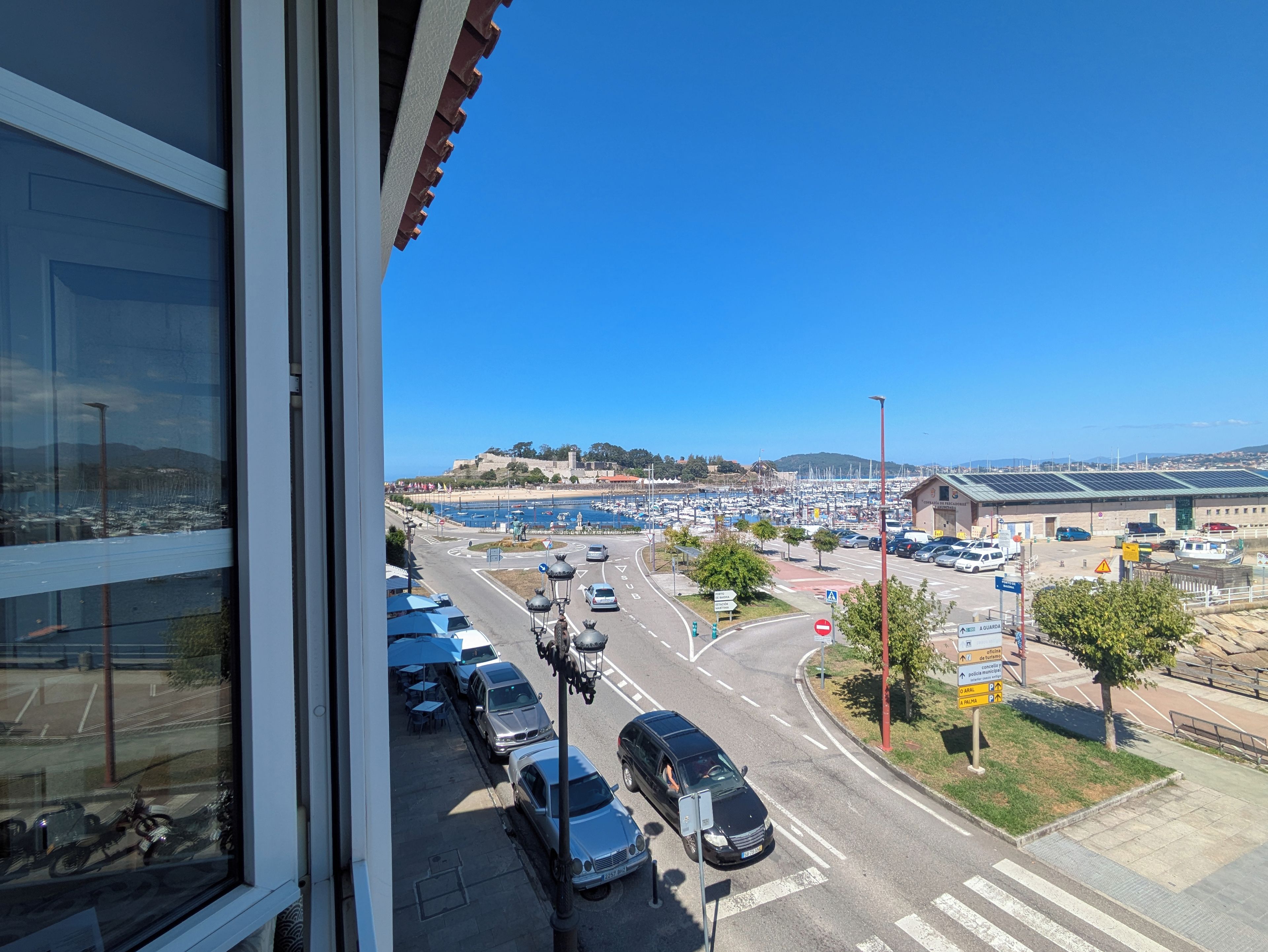 A parking lot with cars, a road, and a view of a marina with boats.