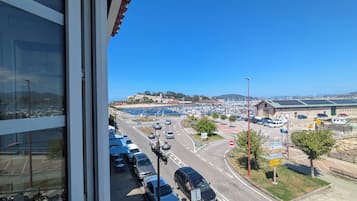 A parking lot with cars, a road, and a view of a marina with boats.