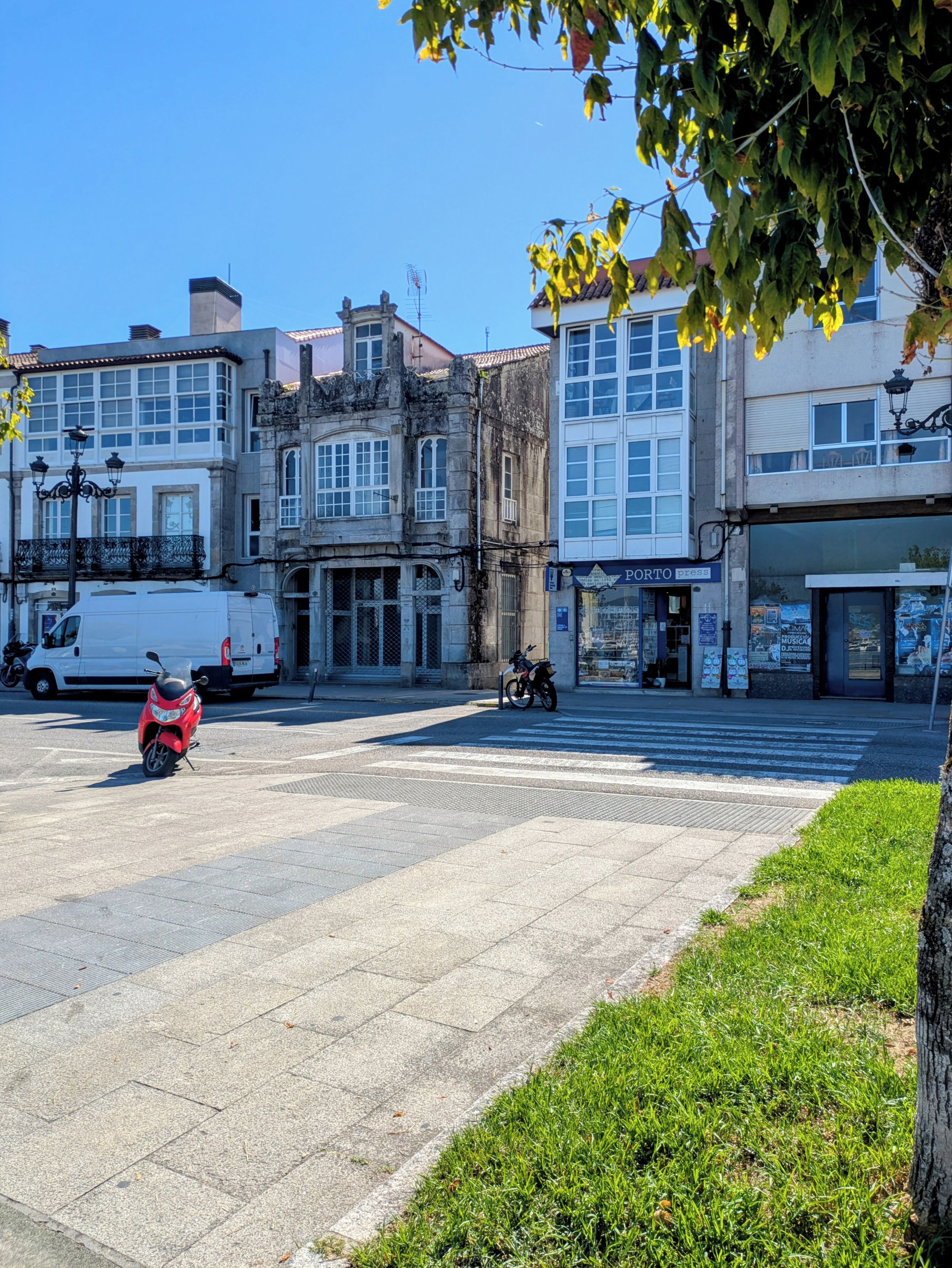 A paved square with a motorcycle parked, surrounded by buildings with various storefronts and a clear blue sky.