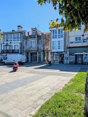 A paved square with a motorcycle parked, surrounded by buildings with various storefronts and a clear blue sky. - Amencer Máxico ~ Downtown • Harbor Views • Parking • Ideal for Couples (Baiona)