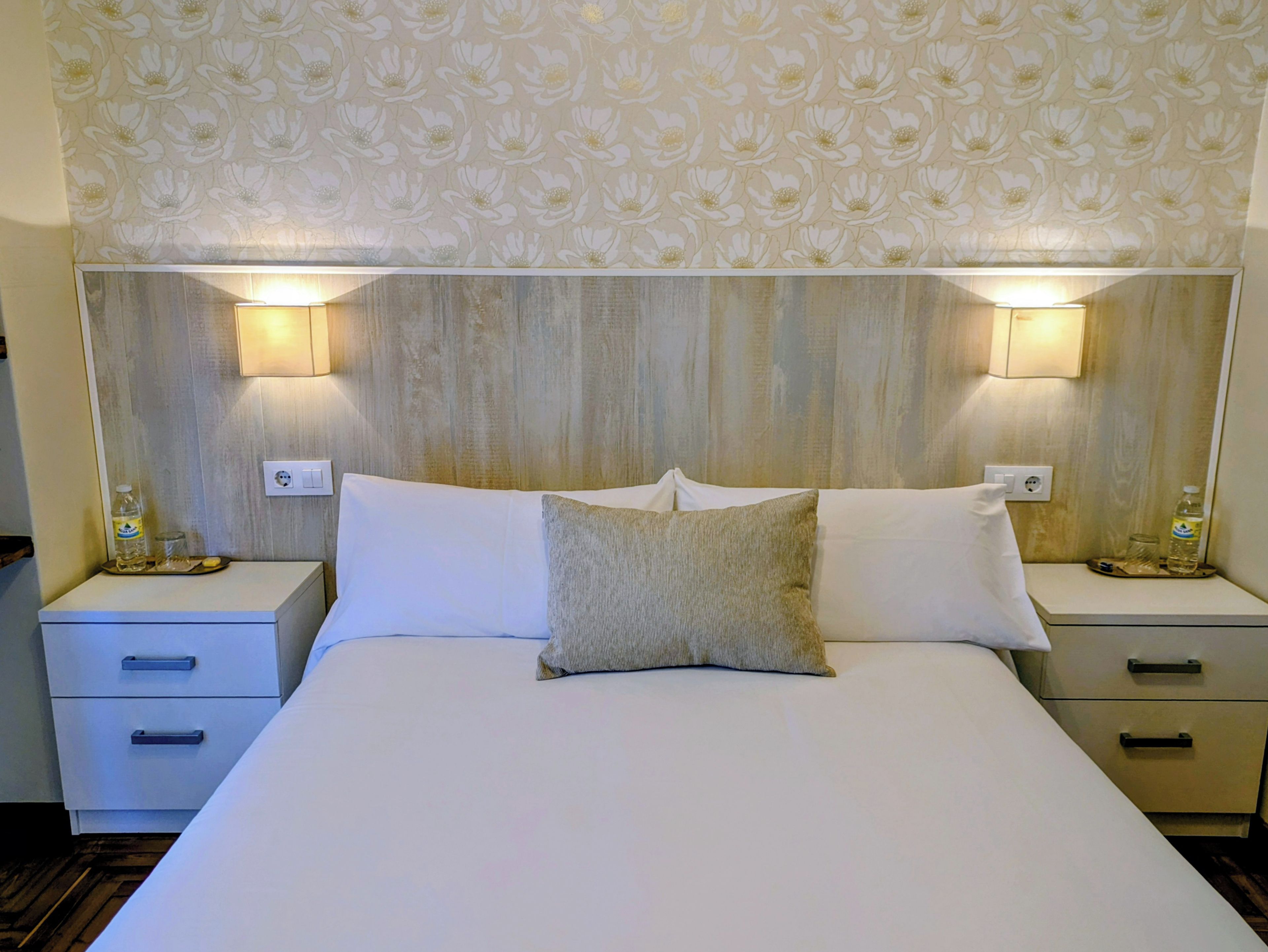 Ein Hotelzimmer mit einem großen Bett, zwei Nachttischen und einem Kopfstück mit Blumenmuster.