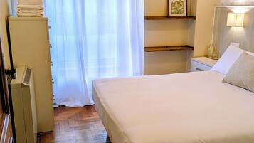 Ein Hotelzimmer mit Bett, Schrank, Nachttisch mit Lampe und einer an der Wand befestigten Ablage mit Bildern.