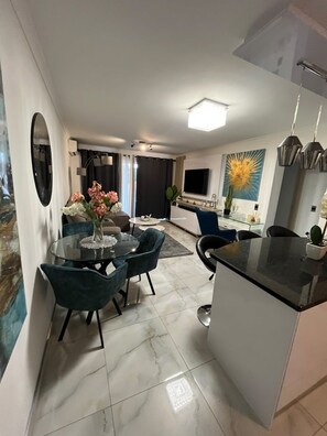 A modern kitchen with a dining area, featuring a round glass table, dark chairs, and a central island. - Stylish Stay with Pools & Gym by Ctha (Cape Town)