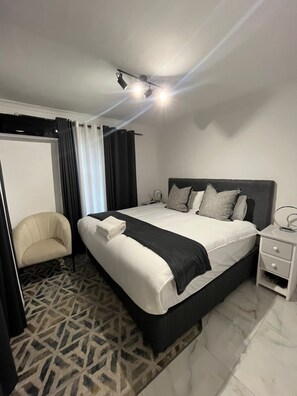Ein Hotelzimmer mit einem großen Bett, einem Nachttisch, einem Sessel und einem gemusterten Teppich.