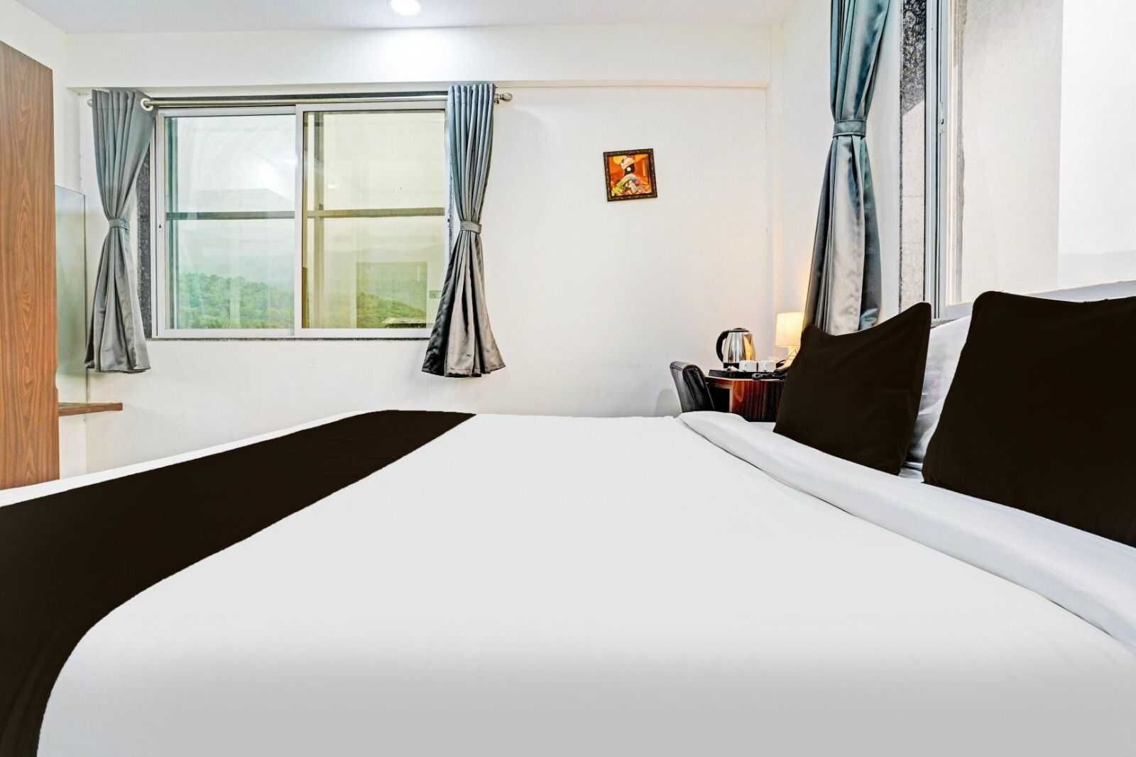 Habitación de hotel con una cama grande, un escritorio con silla, una ventana con cortinas y un pequeño cuadro en la pared.