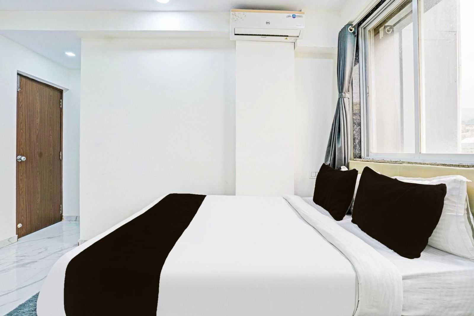Habitación de hotel con cama, ventana con cortinas, unidad de aire acondicionado y puerta de madera.
