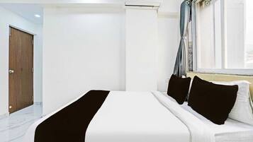 Habitación de hotel con cama, ventana con cortinas, unidad de aire acondicionado y puerta de madera.