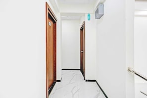 A hallway with white walls, wooden doors, and a marble floor.