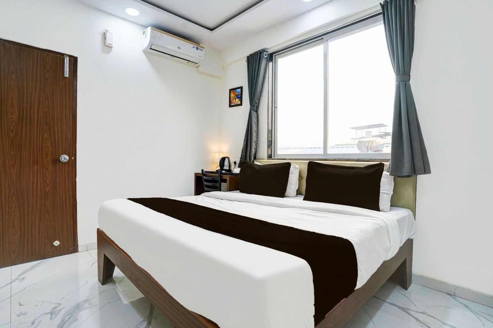 Una habitación de hotel con cama, escritorio, aire acondicionado, ventana con cortinas y puerta.