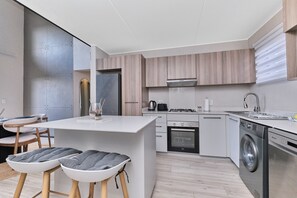 A modern kitchen with a central island, built-in appliances, and a dining area with stools. - Soho Junction Stylish 2-Bed Loft by ctha (Sandton)