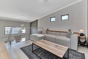 Un salon moderne comprenant un canapé, une table basse, une petite table d’appoint et une fenêtre donnant sur un beau paysage.