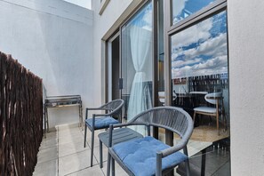 A balcony with two wicker chairs and a small table, a wooden fence, and a glass door leading to an indoor area. - Soho Junction Stylish 2-Bed Loft by ctha (Sandton)